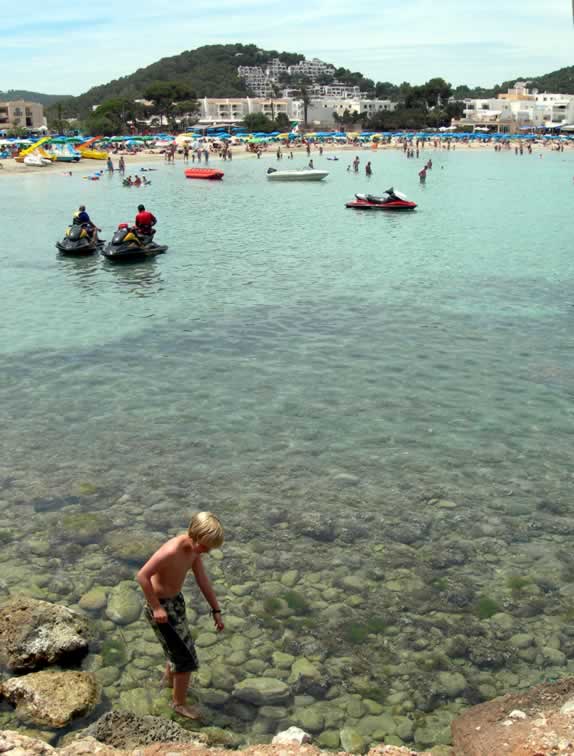 Boy paddling amongst some rocks with Jet skis and small boats behind him